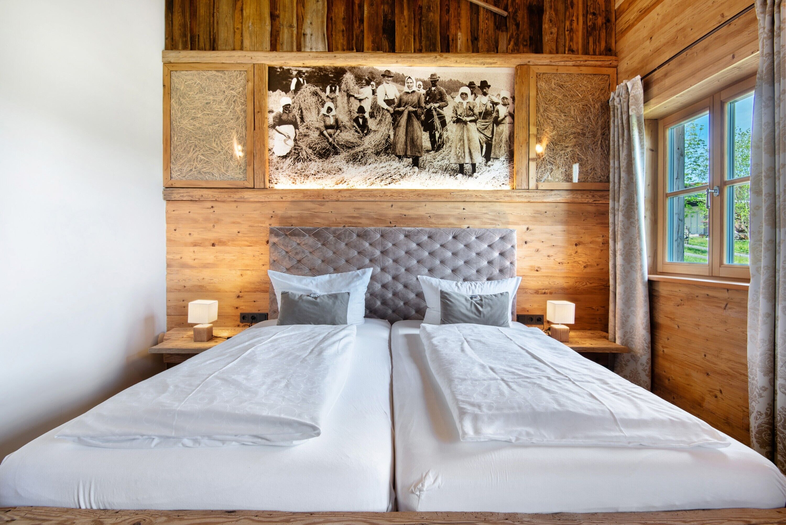 Una cama doble con cabecera capitonada, dos mesitas de noche con lámparas y una fotografía histórica enmarcada sobre la cama.