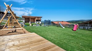 Una terraza de madera, un tobogán y un patio cercado con vistas a colinas distantes.