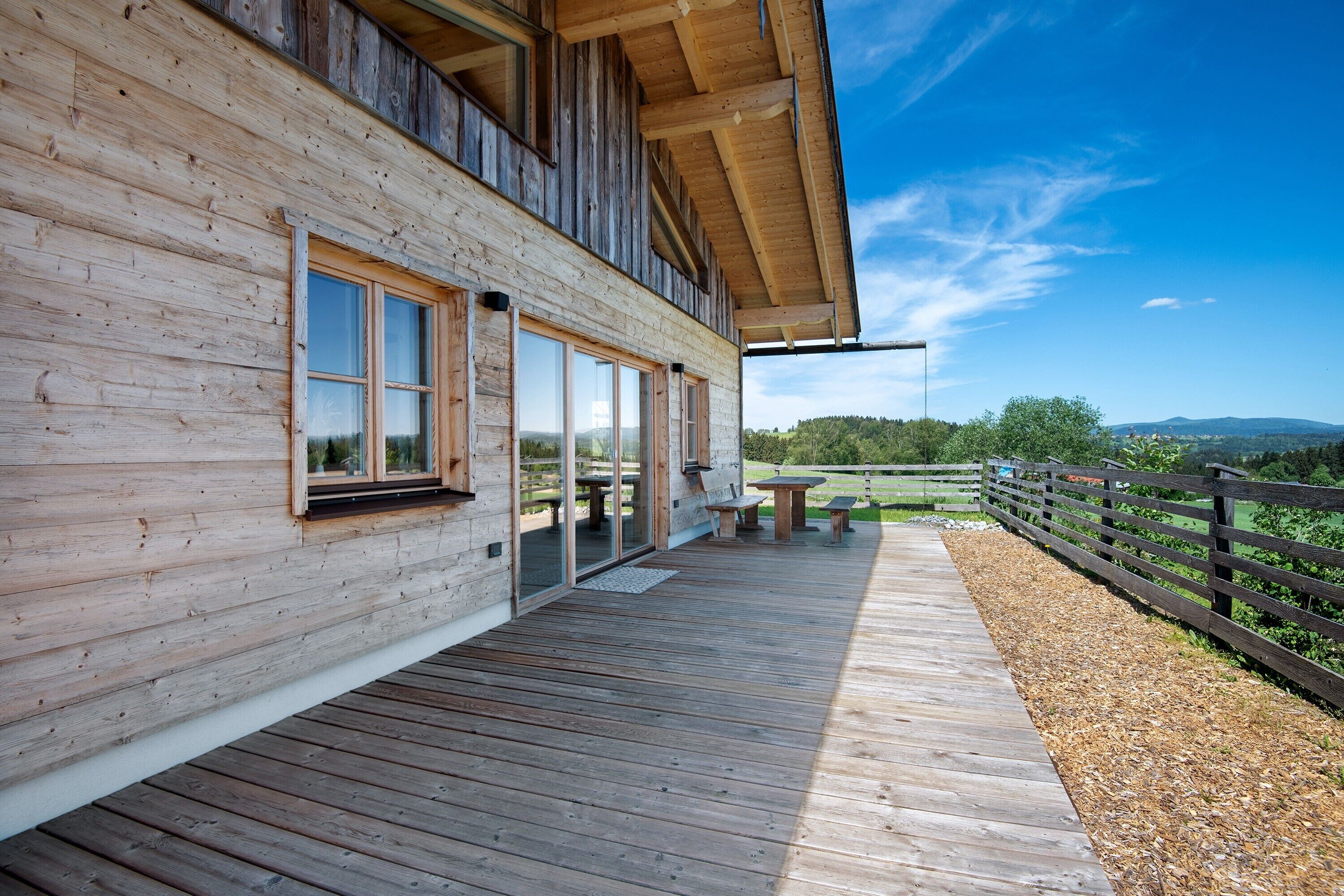 A wooden cabin with a deck, large windows, and a view of the landscape.