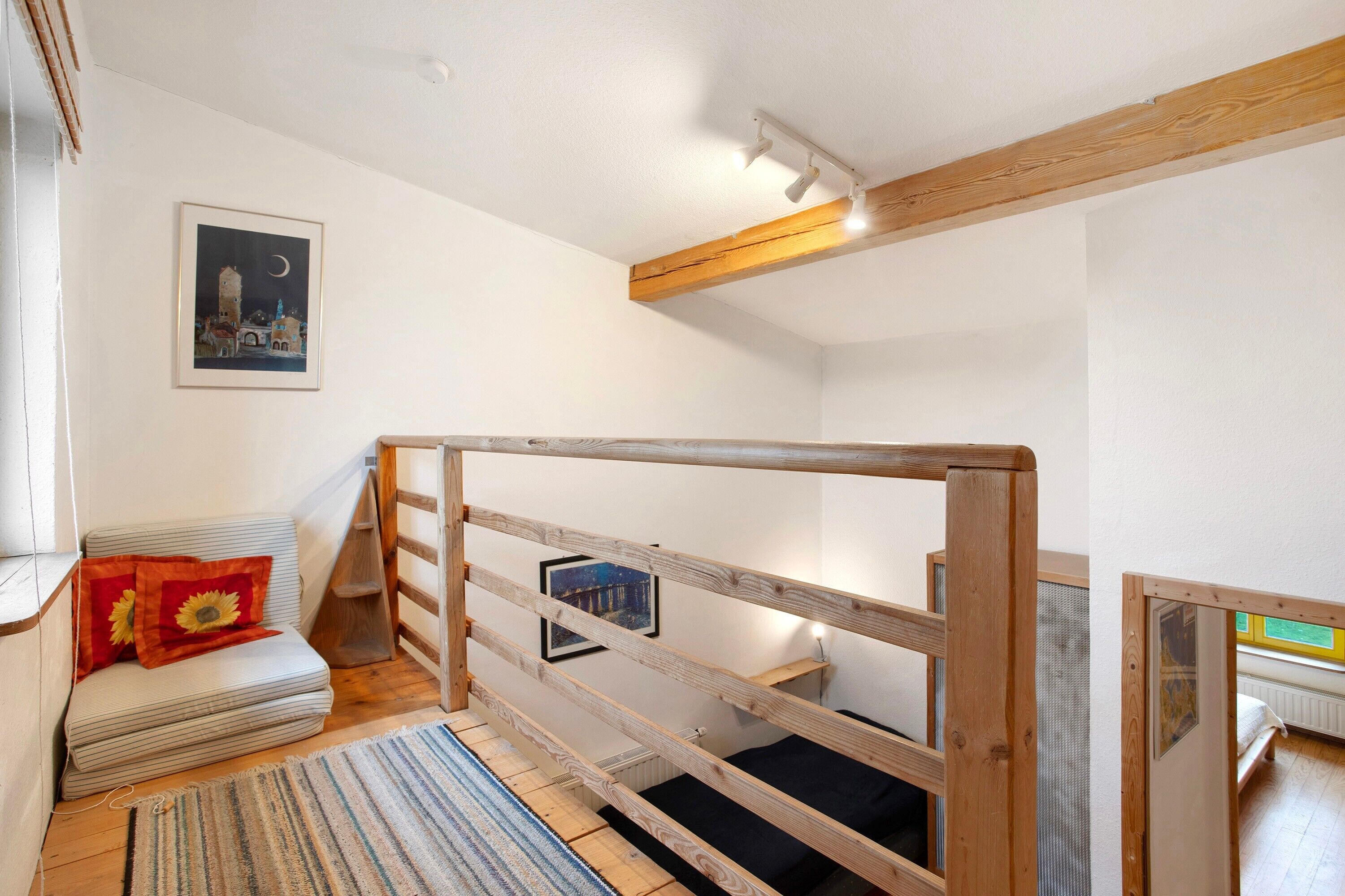 Ein Zimmer mit einem Etagenbett, einem kleinen Sofa mit einem Sonnenblumenkissen, einem gerahmten Bild an der Wand und einer Holzbalkendecke.