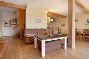 A living room with a wooden floor, a brown leather sofa, a white table, and a dining area with wooden chairs. - Apartment "Poggenkrug Halbsguth" with Lake View, Private Terrace & Wi-Fi (Wolgast)