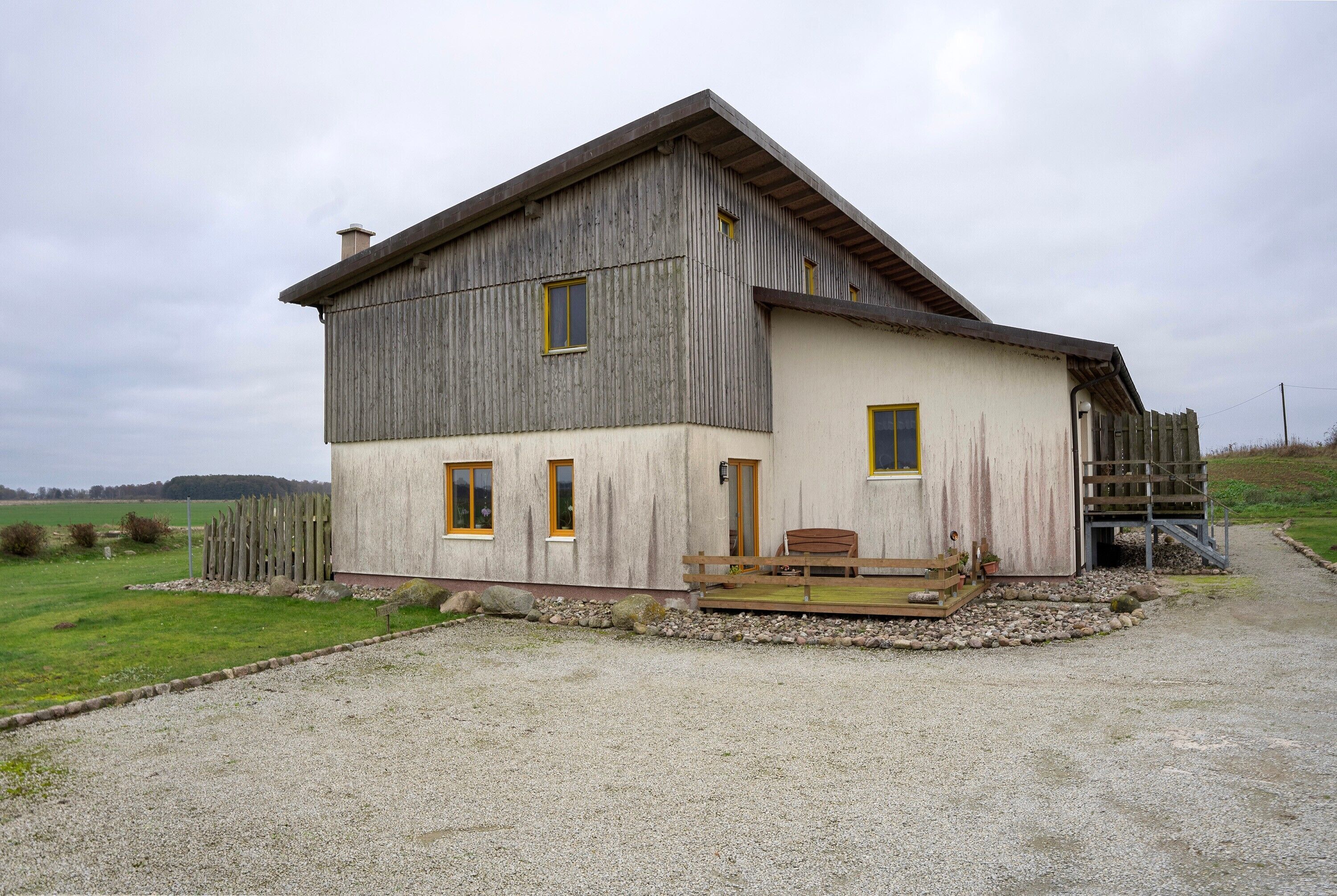 A two-story house with a wooden exterior, a front porch with a bench, and a gravel driveway.