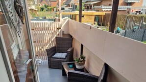 Un balcón con muebles de mimbre, una planta en maceta y vistas a casas vecinas.