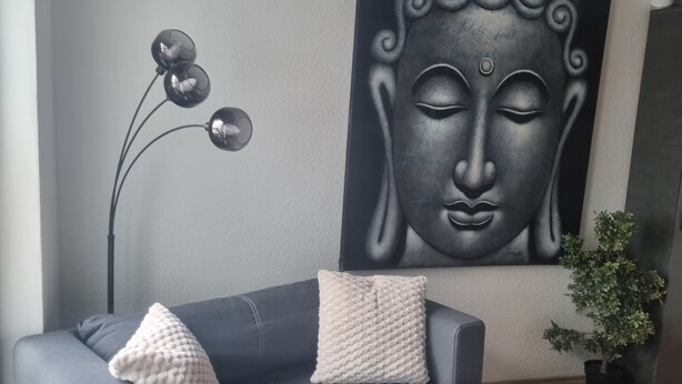 Una sala de estar moderna con un sofá gris, un cuadro de Buda, una lámpara de pie y una planta en maceta.