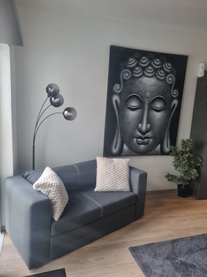 A modern living room with a grey sofa, a Buddha painting, a floor lamp, and a potted plant. - Holiday Apartment 'Kleve Kellen' with Balcony and Wi-Fi (Kleve)
