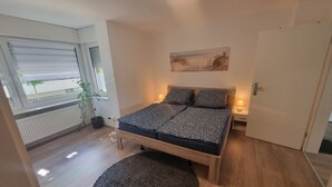 Un dormitorio con cama, ventana, radiador, planta y puerta.