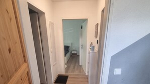 Un pasillo que conduce a un dormitorio con una puerta de madera, un felpudo con texto y vista al interior de la habitación.