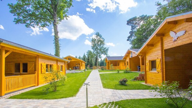 A row of wooden cabins with a paved walkway between them, surrounded by green grass and trees. - Holiday Home 'Ferienhäuser Familie Täubert' with Private Terrace, Private Garden and Wi-Fi (Boxberg/O.L.)