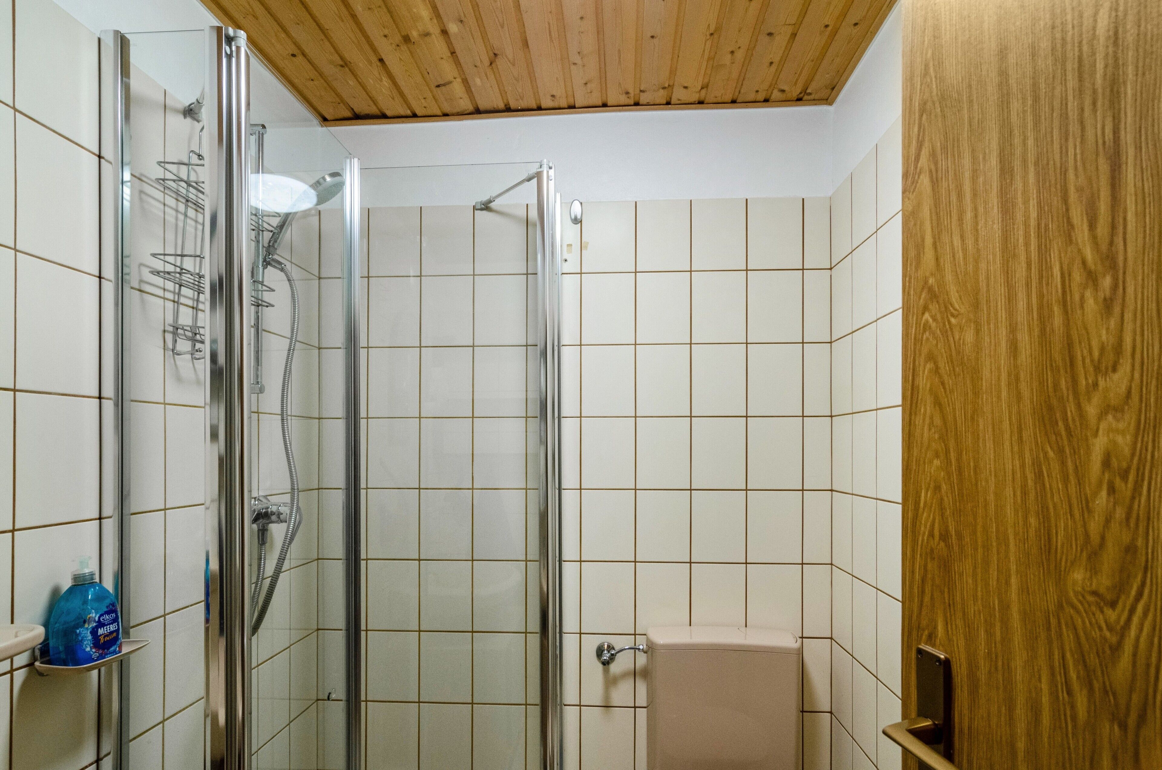 Een douche met een glazen deur, een houten plafond en betegelde wanden.