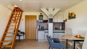 Una cocina compacta con una escalera de madera, un comedor con dos sillas y una mesa pequeña con manzanas.