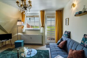 A living room with a sofa, a glass coffee table, a television, a radiator, and a view of the outdoors. - Apartment 'Ruheinsel' with Shared Terrace, Shared Garden and Balcony (Jade)