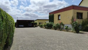 Un camino pavimentado que lleva a un edificio con garaje, rodeado de vegetación y plantas con flores.