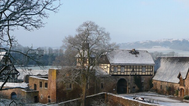 A historic building with a traditional half-timbered facade, a stone archway, and a view of a river in the background. - Holiday flat "Kemenate" - individual flat under the roof (Trendelburg)