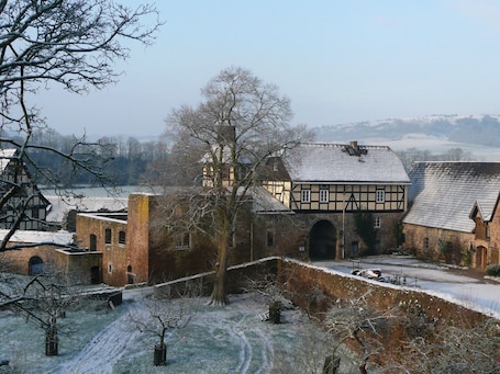 A historic building with a traditional half-timbered facade, a stone archway, and a surrounding moat.. Holiday flat "Kemenate" - individual flat under the roof