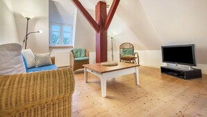 A loft-style living room with a high ceiling, a television, wicker furniture, and a wooden coffee table. - Holiday flat "Kemenate" - individual flat under the roof (Trendelburg)