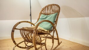 A wicker rocking chair with a cushion in a room with wooden flooring and a white wall. - Holiday flat "Kemenate" - individual flat under the roof (Trendelburg)