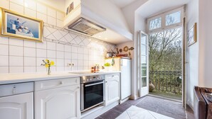 Una cocina moderna con muebles blancos, horno integrado y un amplio ventanal con vistas a un balcón.