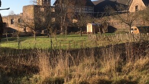 Un edificio histórico con una torre destacada, rodeado por una zona vallada con vegetación escasa.