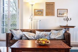 Un salón con un sofá de cuero marrón, una mesa de centro de madera con un frutero, una lámpara de pie y cuadros en la pared.