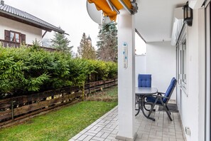 A patio with a table and chairs, a wooden fence, and a building with a tiled roof in the background.