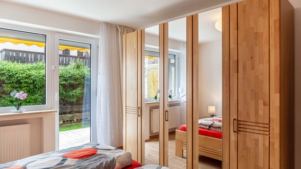 A bedroom with a bed, a wooden wardrobe, a window with curtains, and a view of a garden. - Apartment 'Ferienwohnung Alpenglück' with Mountain View, Terrace and Wi-Fi (Mittenwald)
