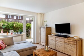 A living room with a sofa, TV, wooden cabinet, and a window overlooking a garden.