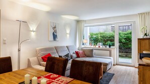 A modern living room with a sofa, dining table, and chairs, a floor lamp, and a view of greenery outside. - Apartment 'Ferienwohnung Alpenglück' with Mountain View, Terrace and Wi-Fi (Mittenwald)