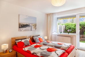 A bedroom with a bed, bedside tables, a clock, a window with a view of greenery, and a painting on the wall.