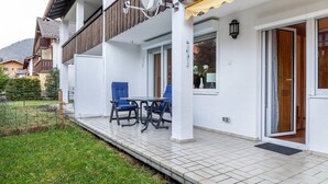 A white building with a balcony, a table, and two chairs. - Apartment 'Ferienwohnung Alpenglück' with Mountain View, Terrace and Wi-Fi (Mittenwald)