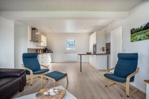 Une cuisine moderne avec des meubles blancs, une table à manger et deux chaises bleues.
