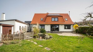 Ein zweistöckiges Haus mit rotem Ziegeldach, einem kleinen Garten mit trittsteinförmigen Wegen und einem Holzzaun.