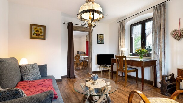 A living room with a sofa, a glass coffee table, a dining table, and a chandelier. - Apartment "Buchhaus Vier - Mittelgeschoss" with Shared Terrace & Wi-Fi (Kirchenlamitz)