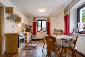 Une cuisine compacte dotée d’un four encastré, d’une table à manger avec des chaises et d’une fenêtre ornée de rideaux rouges.