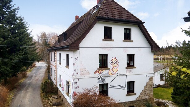 Une maison à deux étages avec un toit brun, un jardin et une route menant à celle-ci.