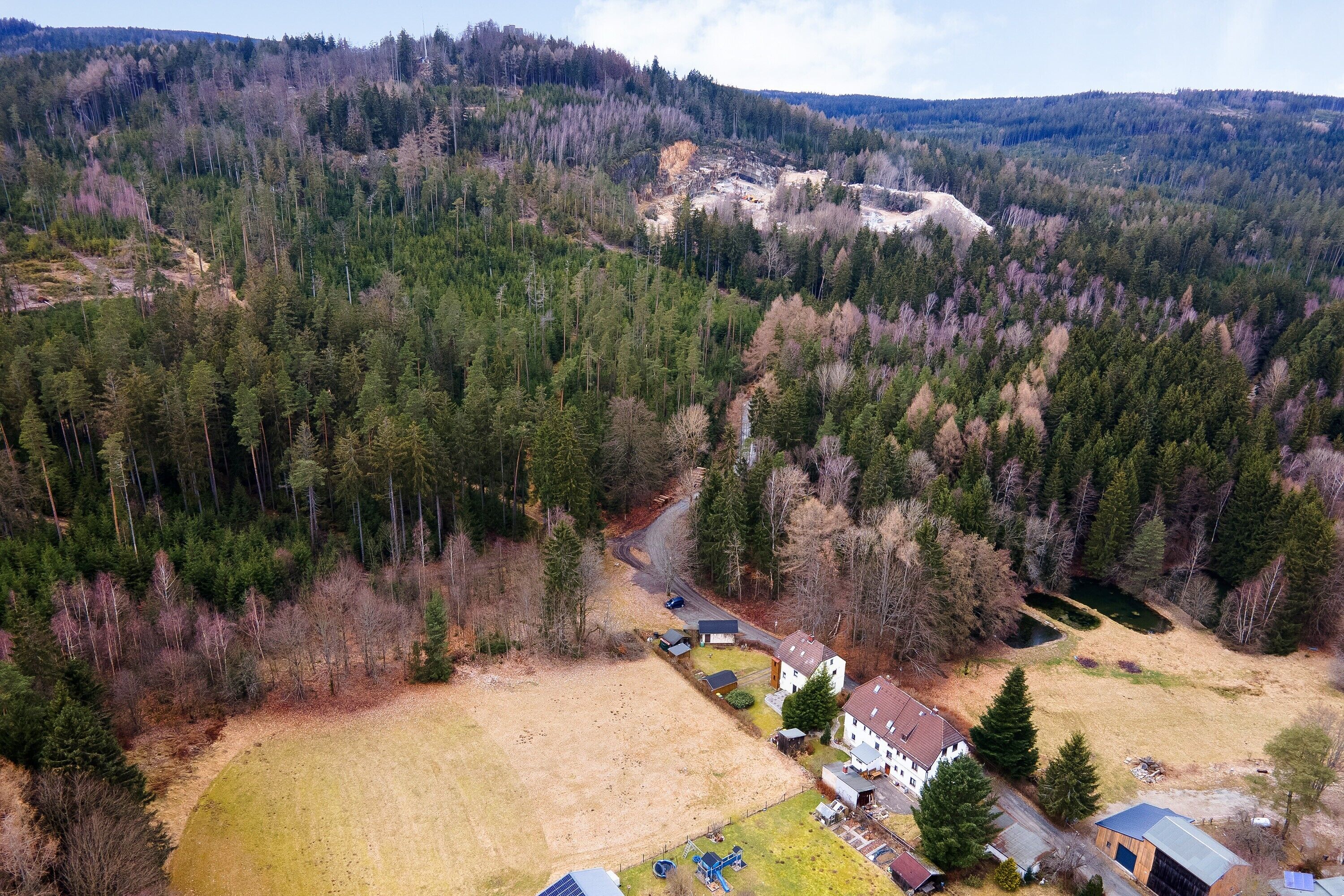 An aerial view of a residential area with houses, a road, and a forested hill.