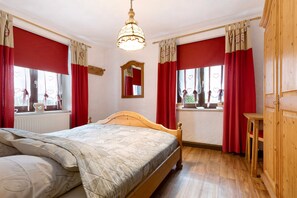 A bedroom with a wooden bed, red curtains, a window with a view, a wooden dresser, and a hanging light fixture. - Apartment "Buchhaus Vier - Erdgeschoss" with Shared Terrace & Wi-Fi (Kirchenlamitz)