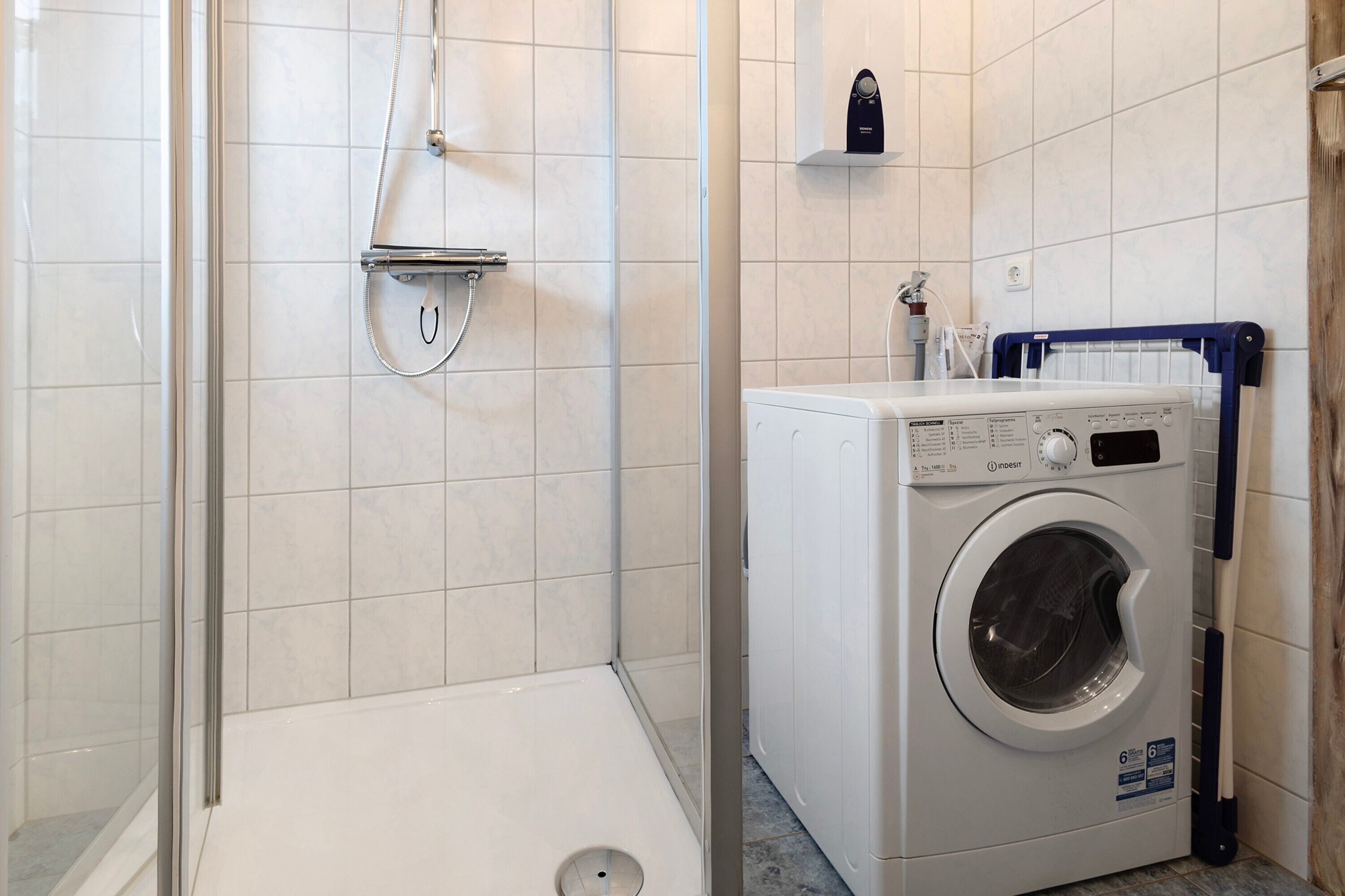 Un espace buanderie comprenant un lave-linge, une douche et un mur carrelé.