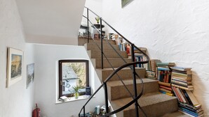 Un escalier avec une rampe en métal, une fenêtre donnant sur un immeuble et une pile de livres posée sur les marches.