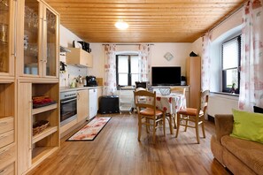 Eine kleine Küche mit Holzausstattung, ein Essbereich mit Stühlen, ein Fernseher und ein Sofa mit grünem Kissen.