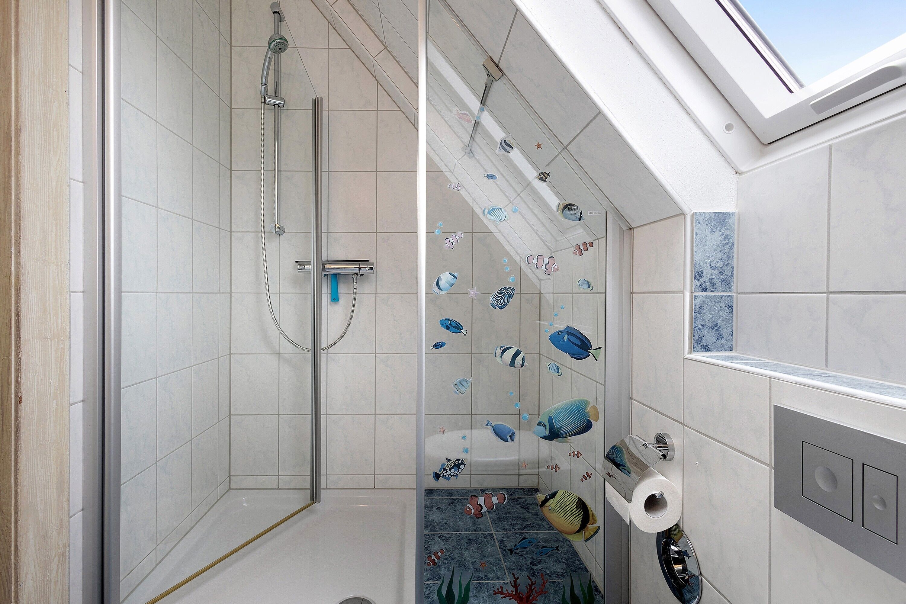 Een moderne badkamer met een douchecabine van glas, een toilet met een papieren handdoekdispenser en een dakraam.