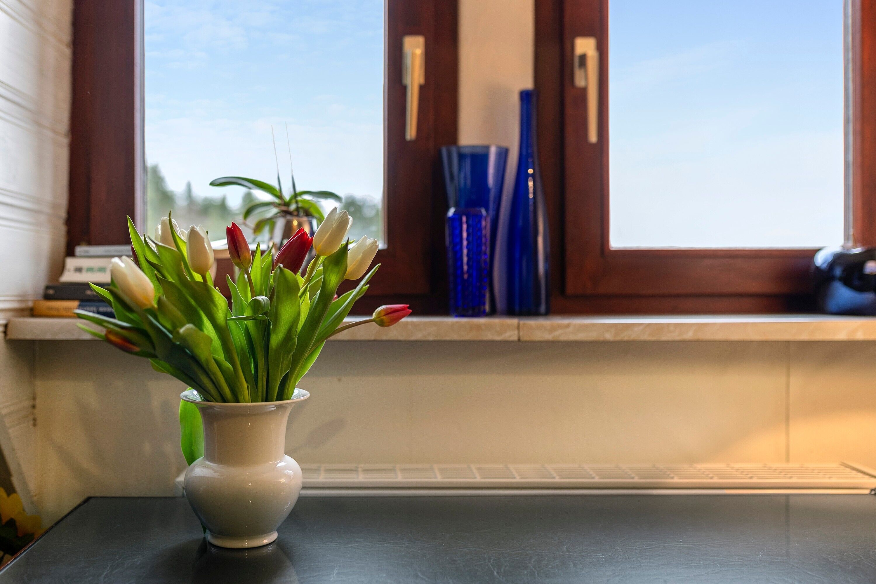 Un jarrón blanco con tulipanes sobre una mesa cerca de una ventana con vistas.