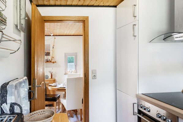 A compact kitchen with a stove, a refrigerator, and a dining area visible through an open door.