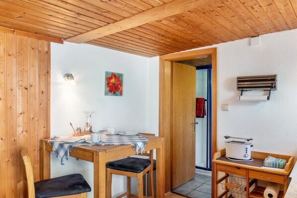 A wooden interior with a dining table, chairs, a small kitchen area with a toaster, and a door leading to another room.