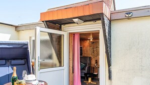 Una habitación con techo de madera, una puerta que da a un balcón, una mesita con una botella, un vaso y un sombrero.