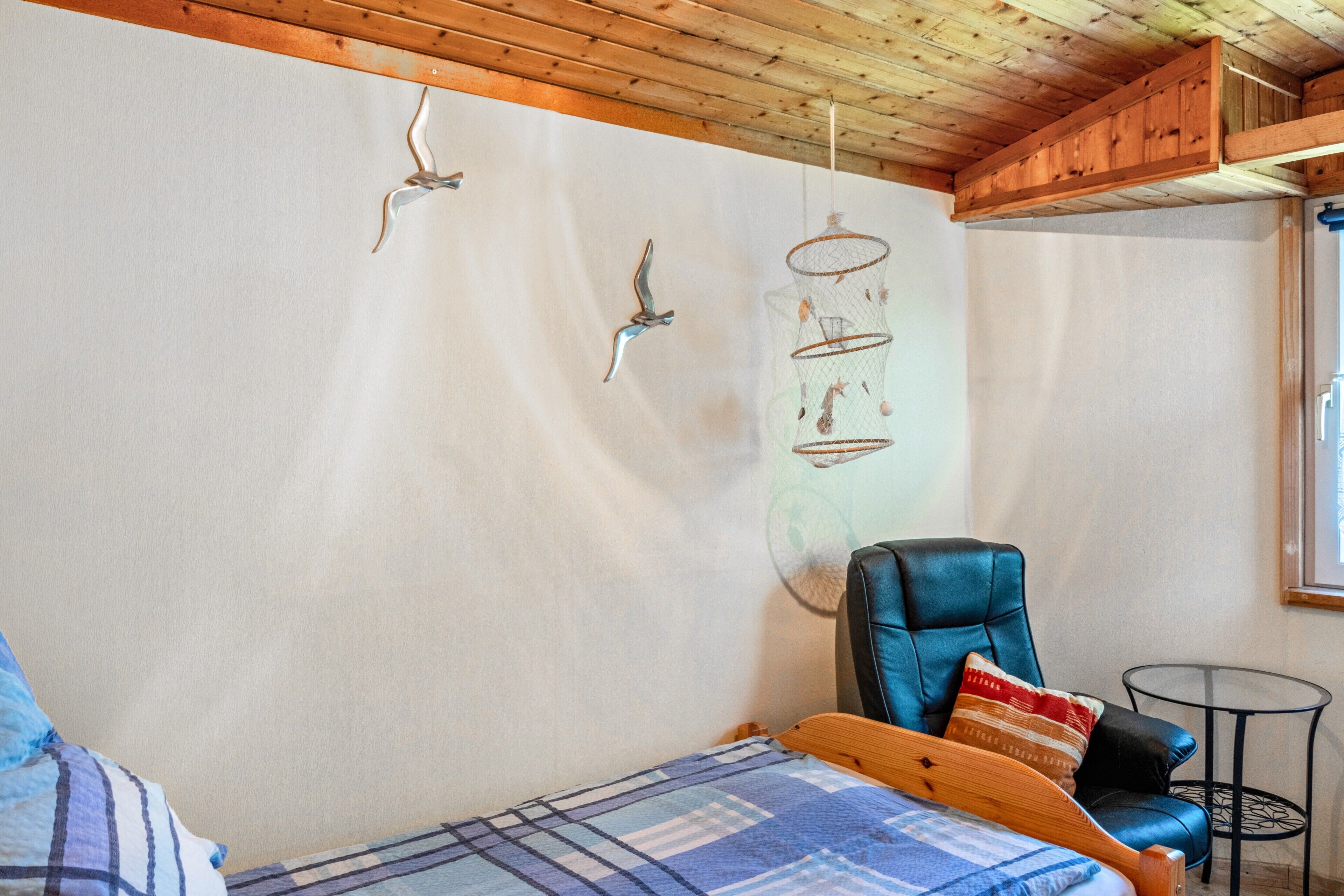 Ein Zimmer mit einem Bett, einem blauen Ledersessel, einem kleinen runden Tisch und an der Wand befestigten Vogelkäfigen.