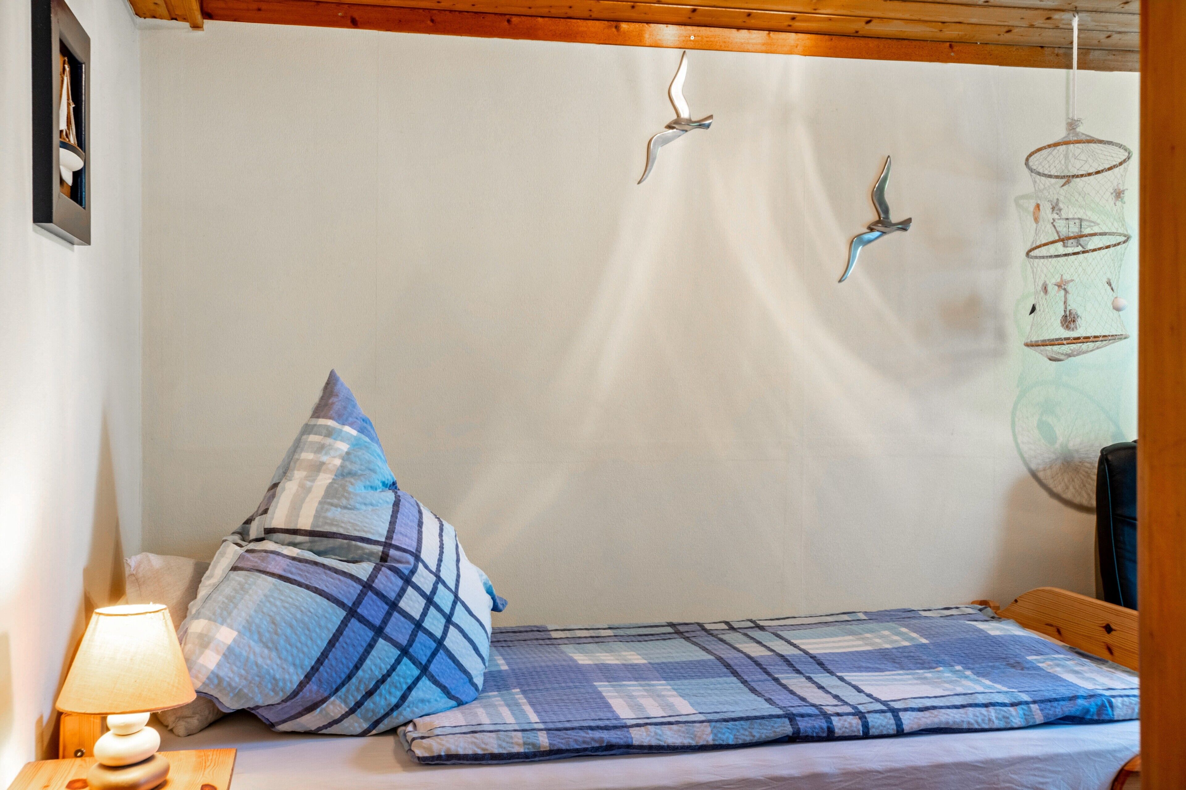 Ein kleines Bett mit karierter Decke, einer Nachttischlampe und Wandkäfigen für Vögel.