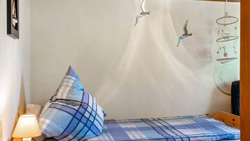 Ein kleines Bett mit karierter Decke, einer Nachttischlampe und Wandkäfigen für Vögel.