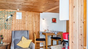 Una habitación con paneles de madera, una mesa de comedor, sillas, una cafetera y un sillón gris con un cojín amarillo.