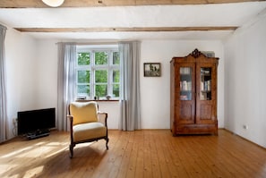 A room with wooden flooring, a television, a chair, a cabinet, and a window with curtains.