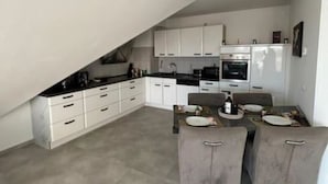 A modern kitchen with white cabinets, a dining area with grey chairs, and a built-in oven. - Apartment 'Maisonette Wohnung Frechen City' with Private Terrace, Wi-Fi and Air Conditioning (Frechen)